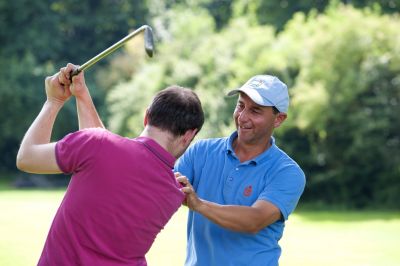 Ein Golflehrer zeigt einem Anfänger wie er sich beim Schlag richtig hinstellen muss.